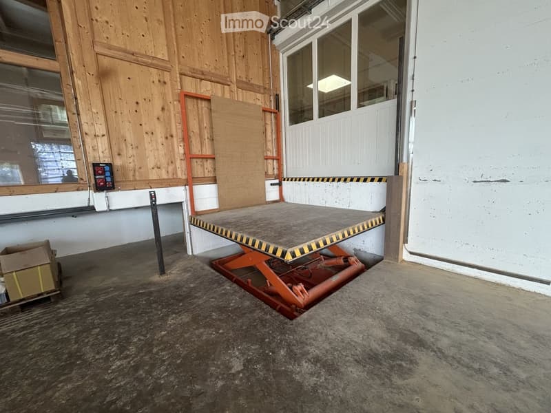 Empty room with a raised ground floor, wooden walls, and a large window. A ramp is visible leading to the raised area.