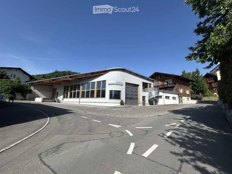 Modern industrial-style building with large windows and a garage entrance, surrounded by trees and other residential structures.