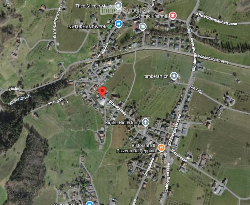A satellite view of a rural area showing a small village with scattered buildings, roads, and green fields.
