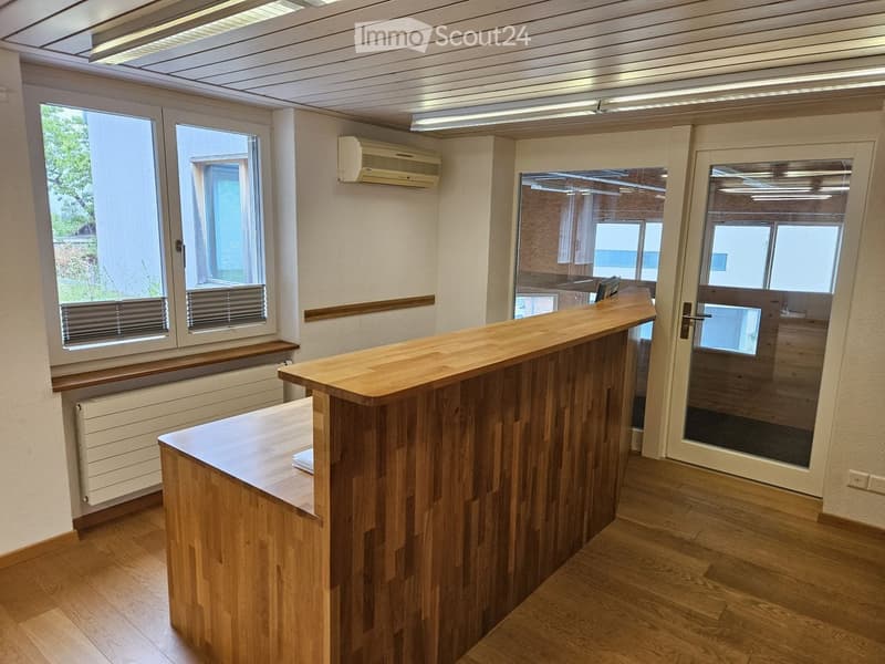 Bright, modern reception area with a wooden reception desk, large windows, and an air conditioning unit on the wall.