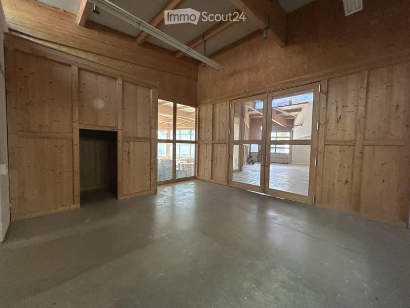 Empty room with wooden walls, exposed wooden beams, large windows, and a concrete floor.