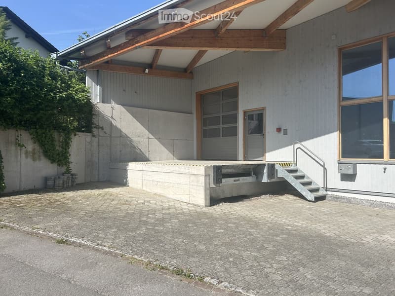 Modern two-story building with a raised ground floor, garage, and large windows. The entrance features a small staircase leading up to a covered porch area.