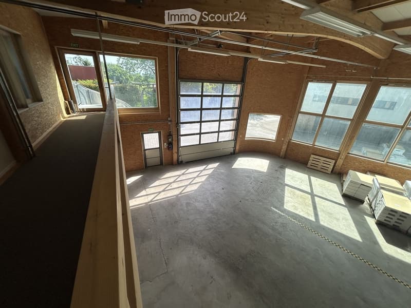 Empty industrial-style room with exposed wooden beams, large windows, and a concrete floor. No furniture or equipment present.