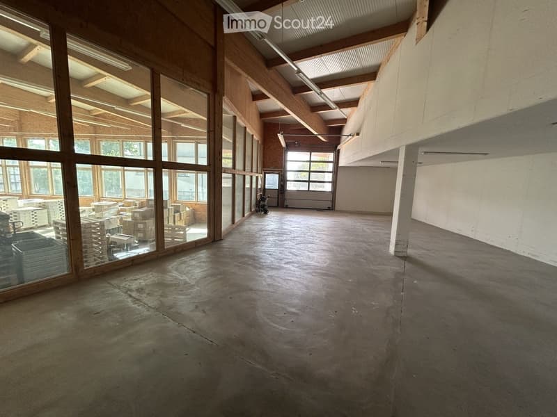 Empty room with concrete floor, large windows, wooden beams, and a garage door at the back.