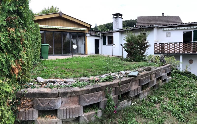 Two-story house with a modern design, featuring a large glass sliding door, a chimney, and a well-maintained garden with a stone retaining wall.