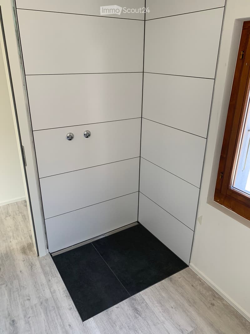 Empty room with light grey cabinetry, black floor tile, and wooden flooring.