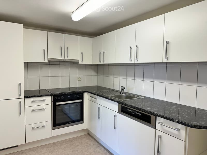Modern kitchen with white cabinets, black granite countertops, built-in oven, and stainless steel sink.