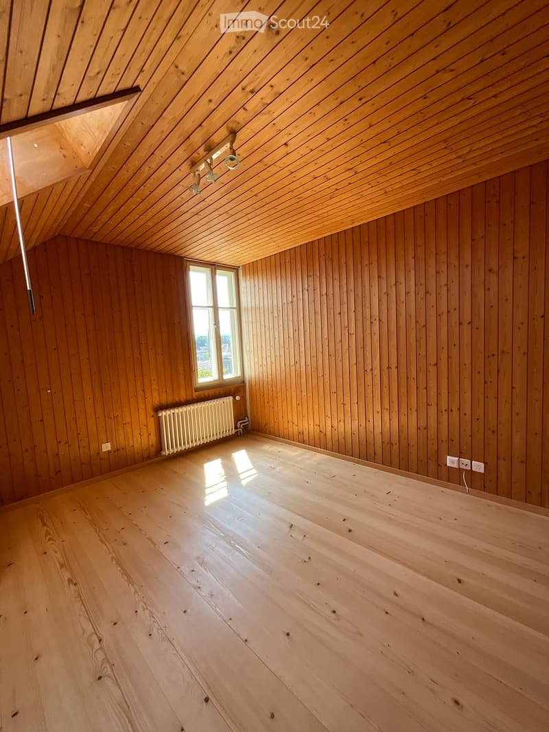 Empty room with wooden walls, wooden floor, and a small window letting in natural light. The room features exposed wooden beams on the ceiling and a radiator on one wall.