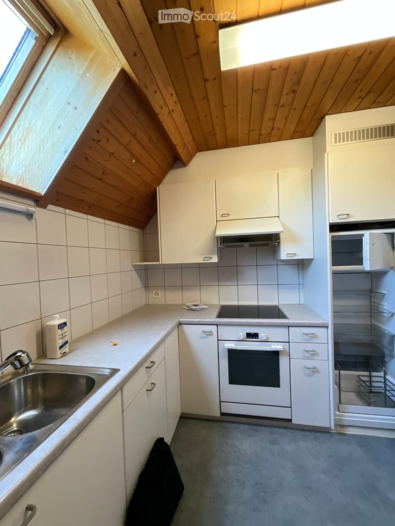 Modern kitchen with white cabinets, stainless steel sink, oven, and refrigerator. Wooden slanted ceiling and tiled walls.