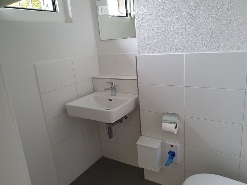 small bathroom with white tiles, a white sink, silver faucet, mirror, toilet, and a white towel holder