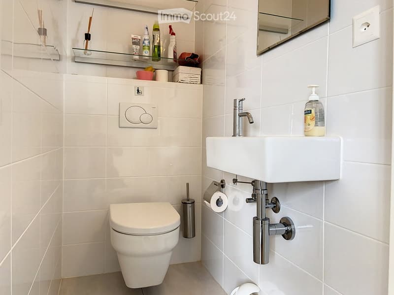 Bathroom. Modern bathroom with white tiles, a toilet, a sink with a chrome faucet, a mirror, and a glass shelf holding toiletries.