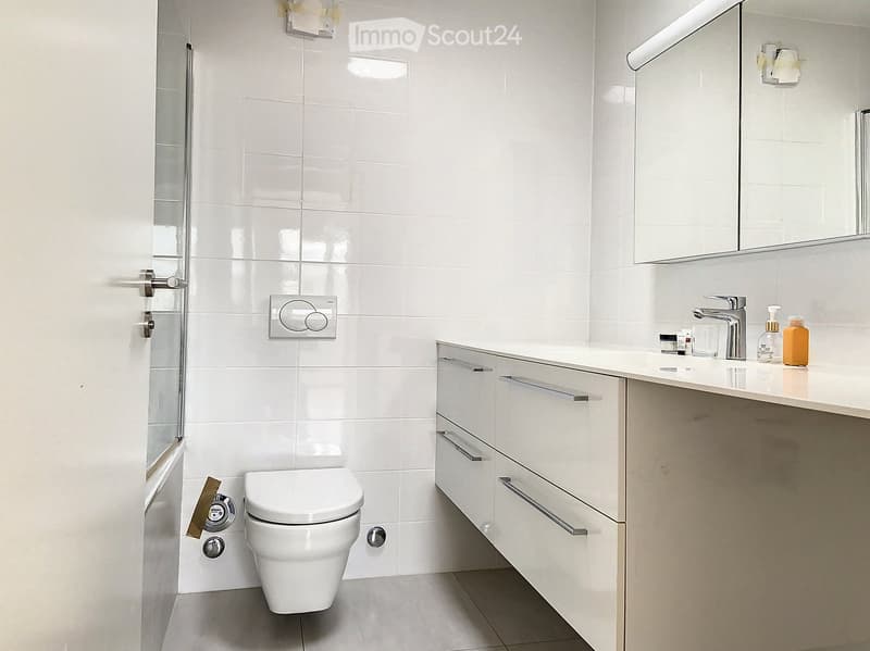 Bathroom. Modern bathroom with white tiles, a toilet, a sink with a modern faucet, a large mirror, and a cabinet with silver handles.