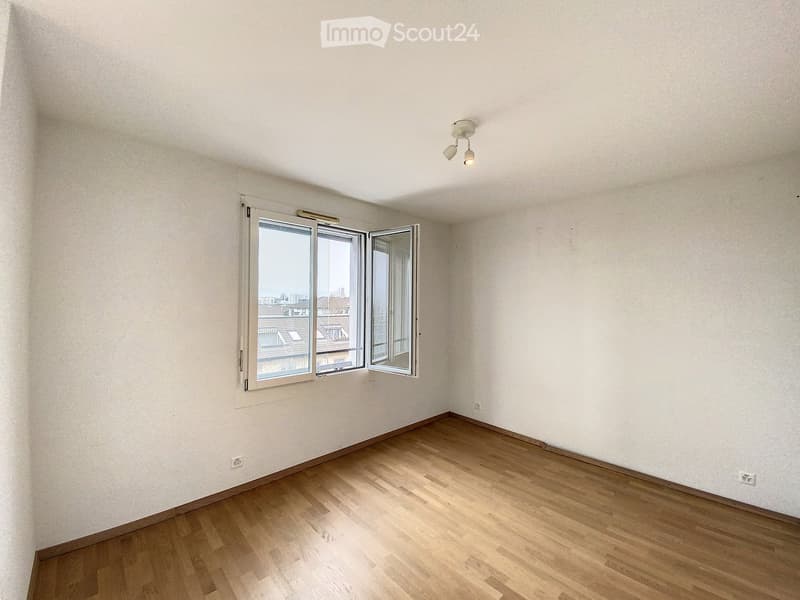 Unfurnished Room. Empty room with wooden flooring, white walls, and large windows offering a cityscape view. No furniture or equipment present.