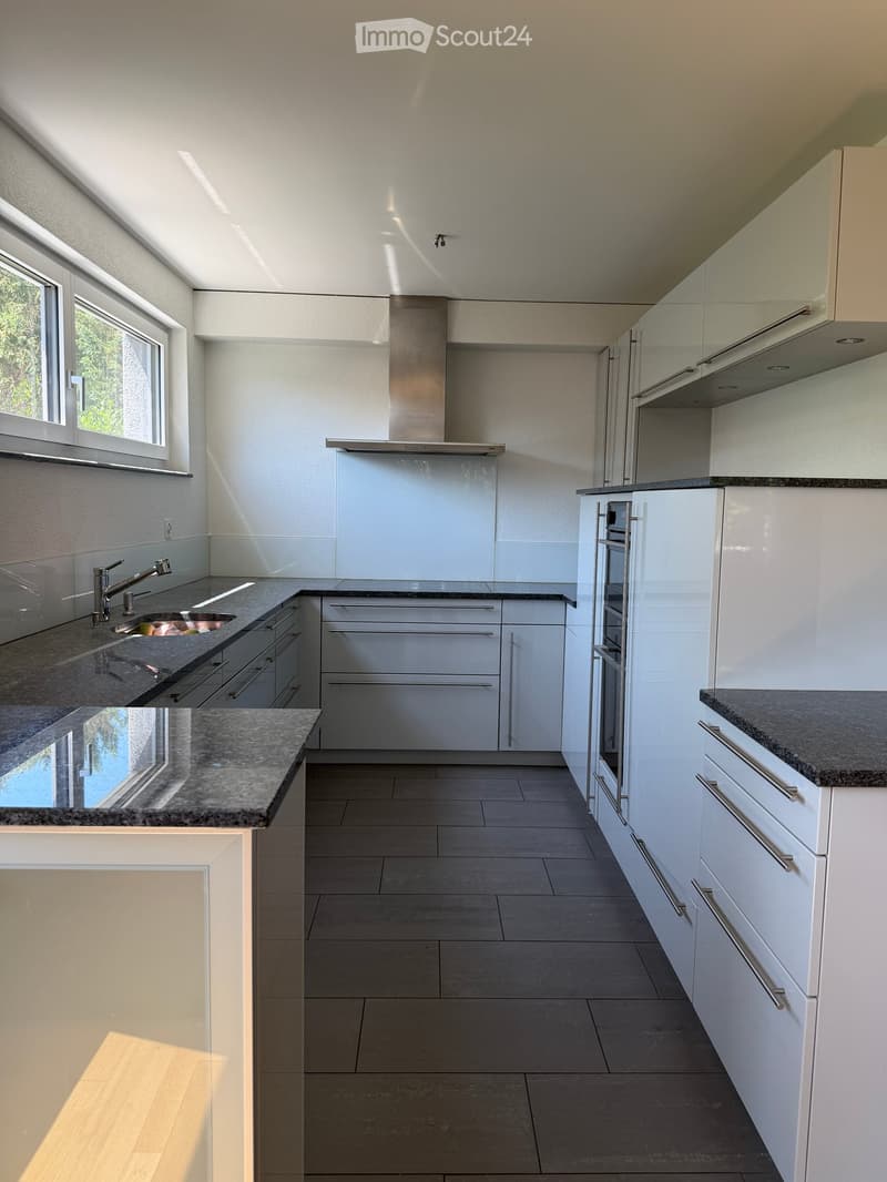 Modern kitchen with white cabinets, granite countertops, stainless steel appliances, and large windows allowing natural light.
