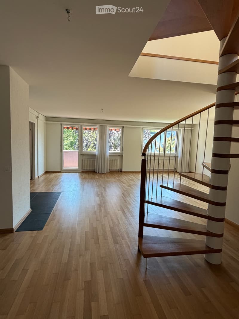 Empty hallway with wooden flooring, a curved staircase, large windows, and a door leading outside.
