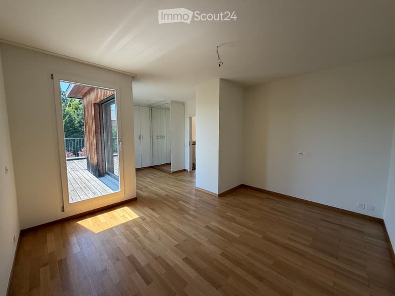 Empty room with wooden flooring, white walls, and a sliding glass door leading to a balcony.