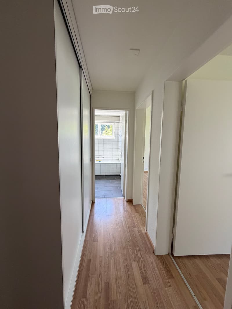 Empty hallway with wooden flooring, white walls, and several open doors leading to other rooms.