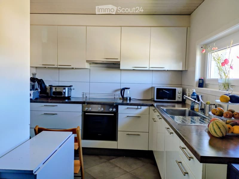 Modern kitchen with white cabinets, stainless steel appliances, and a dark countertop. Includes an oven, microwave, sink, and various small appliances.