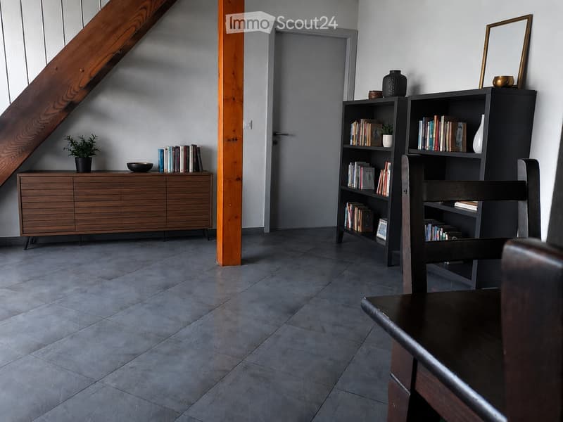 Modern, minimalist room with grey tiled floor, wooden staircase, bookshelf, cabinet, and small plant on a side table.
