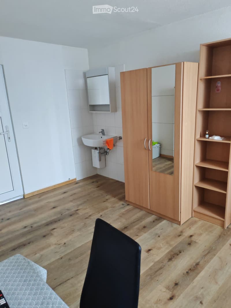 Bathroom with wooden floor, white tiled walls, sink, mirror, wooden cabinet, and shelf with items.