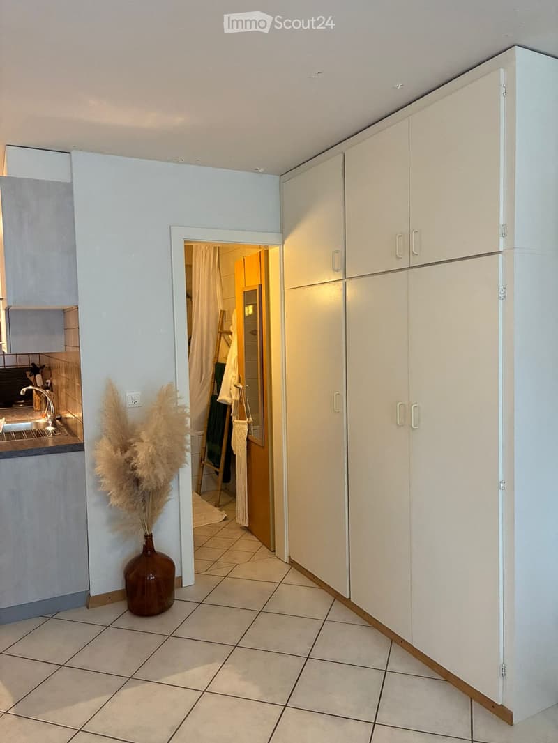 A hallway with white cabinets, a vase with dried plants, and an open doorway leading to a bathroom.