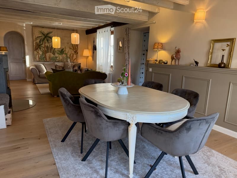 Elegant living and dining area with a green sofa, a white dining table with six chairs, a fireplace, and decorative items on the mantel.