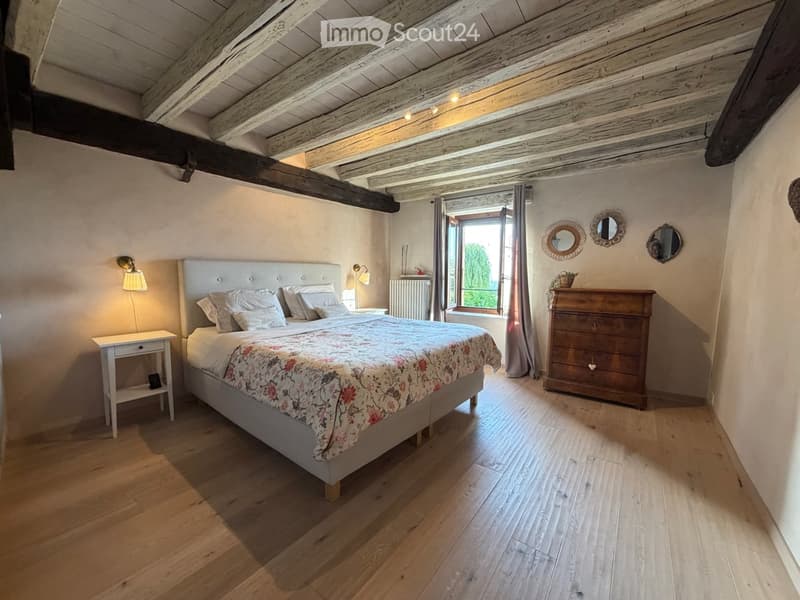 Cozy bedroom with exposed wooden beams, a large bed with floral bedding, a wooden nightstand, a dresser, and wall-mounted mirrors.