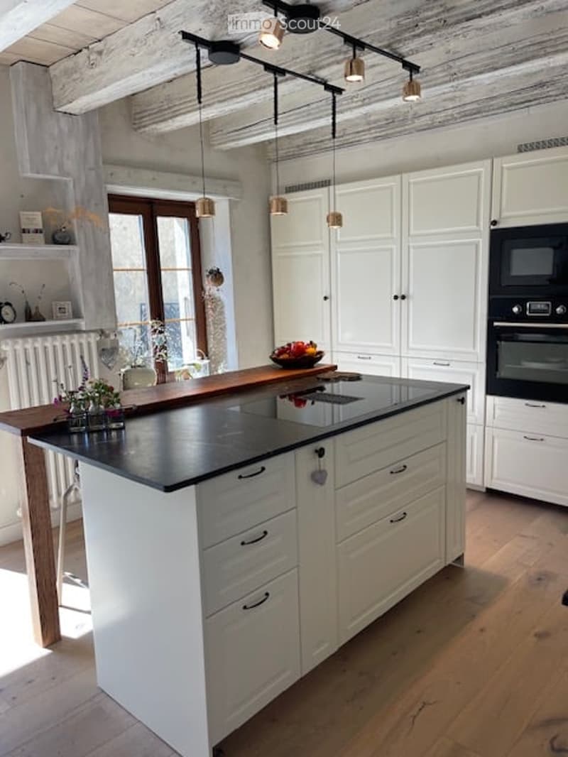 Modern kitchen with white cabinets, a central island with black countertop, induction cooktop, microwave, and pendant lights. The island features a wooden countertop extension and small potted plants.