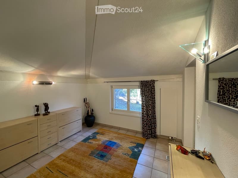 A small, well-lit room with a chest of drawers, a vase, statues, a mirror, a table with keys and sunglasses, and a colorful rug.