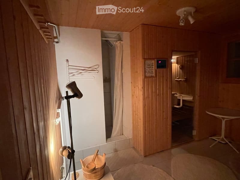 Bathroom with wooden walls and ceiling, a small table, a wooden bucket with wooden spoons, a mirror, a sink, and a shower area with a curtain.