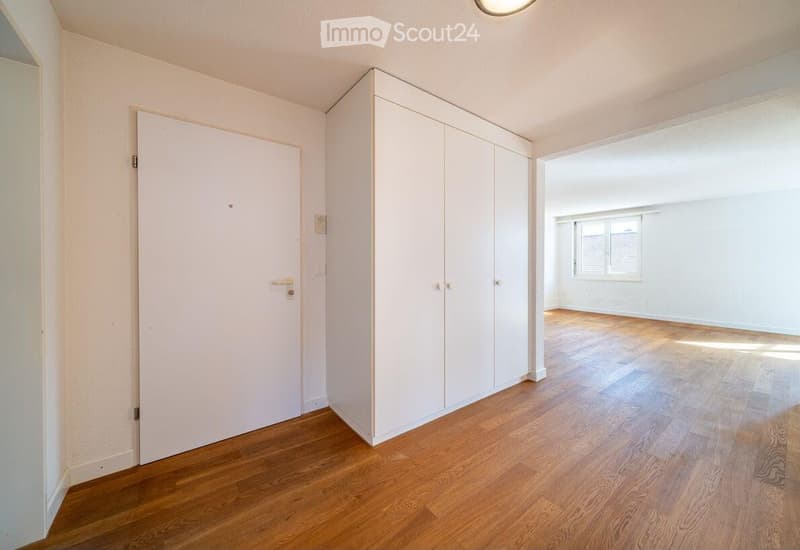 Unfurnished Room. Empty room with wooden flooring, white walls, and a built-in closet. A door leads to another room with a window.