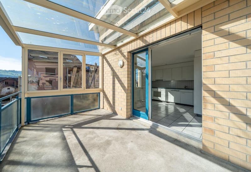 Balcony / Terrace. Balcony with glass roof, sliding glass doors leading to a kitchen area, tiled floor, and view of surrounding buildings.