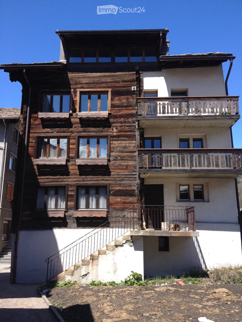 A multi-story wooden house with white walls, multiple windows, balconies, and a staircase leading to the entrance.