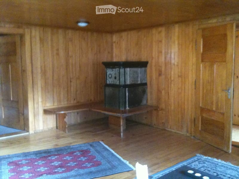 Wooden-paneled room with a built-in bench seating around a central fireplace, two rugs on the floor, and wooden doors.