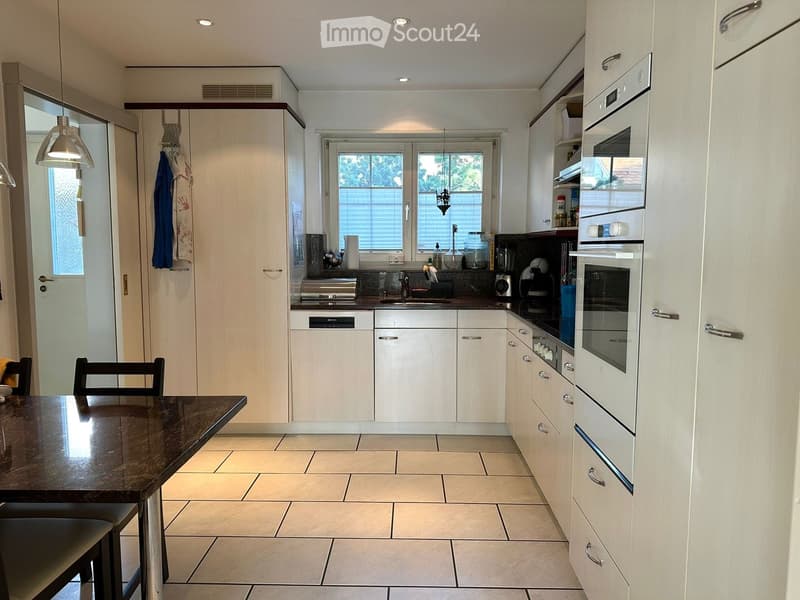 Modern kitchen with white cabinets, granite countertop, built-in oven, dishwasher, and a small dining area with a table and chairs.