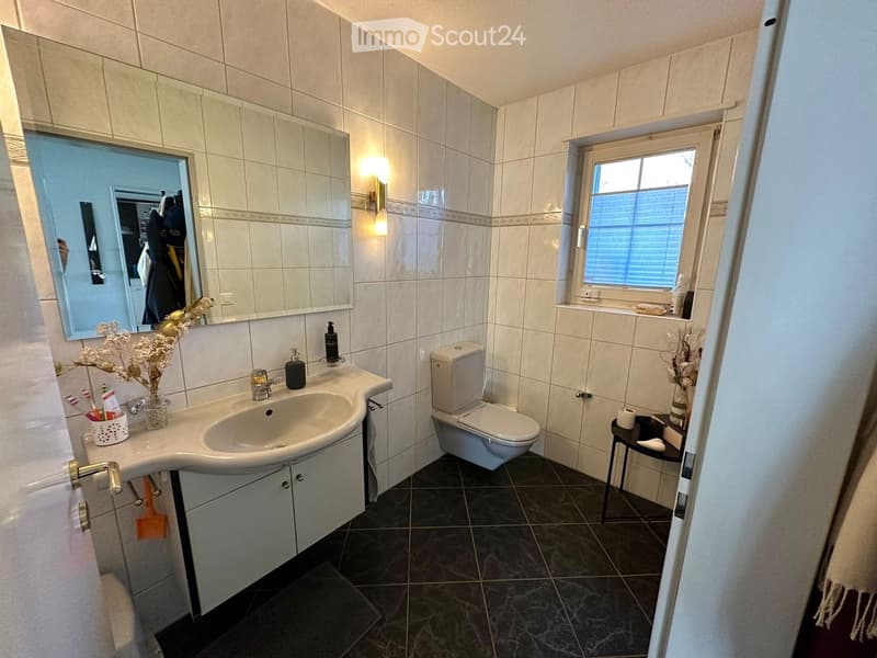 Modern bathroom with a white sink, toilet, large mirror, and a small table with decorative items.