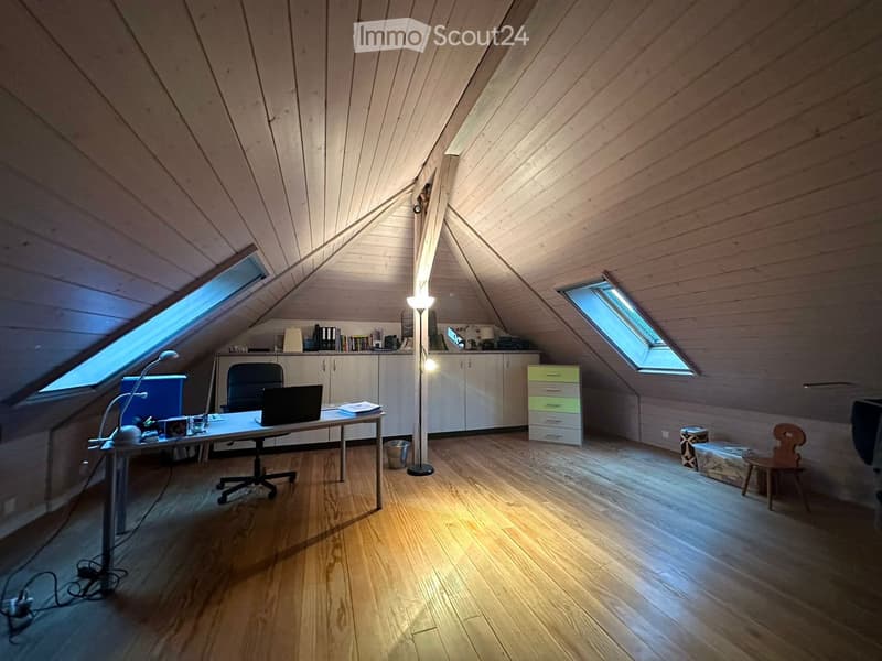 Bright attic room with wooden floors, slanted wooden ceiling, skylights, and a desk setup with a laptop, chair, and floor lamp.