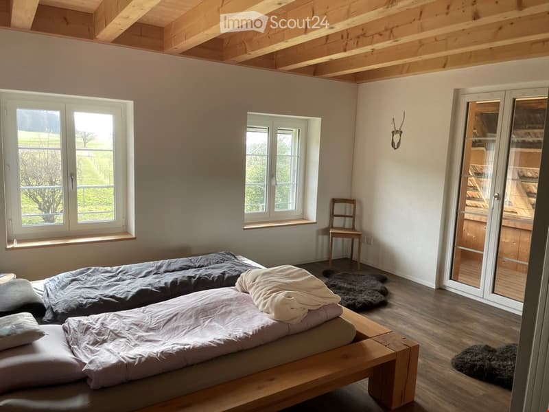 Bedroom. Bright bedroom with wooden floors, large windows, two beds with bedding, a wooden chair, and a small rug.