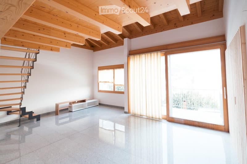 Bright, open space with wooden ceiling beams, a modern staircase, large windows, and a sliding glass door leading to a balcony.
