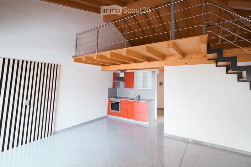 Modern kitchen area with red and white cabinets, stainless steel appliances, and a sleek countertop. The space features a polished concrete floor and a wooden ceiling with exposed beams.