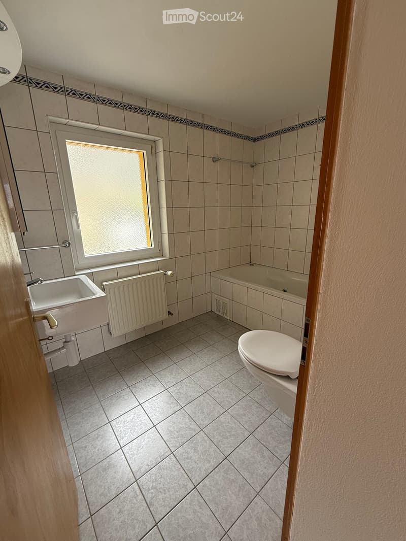 Bathroom with tiled walls and floor, featuring a sink, toilet, bathtub, and radiator. A window provides natural light.