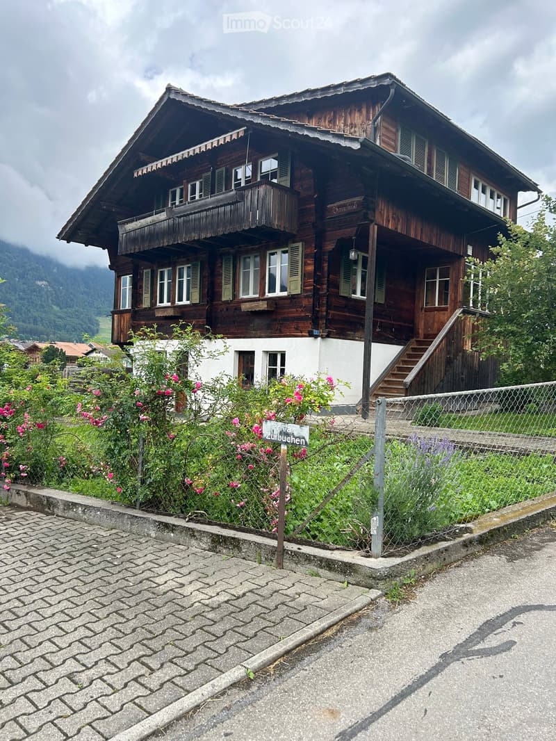 Traditional wooden house with a steep roof, multiple windows, and a balcony overlooking a scenic valley.