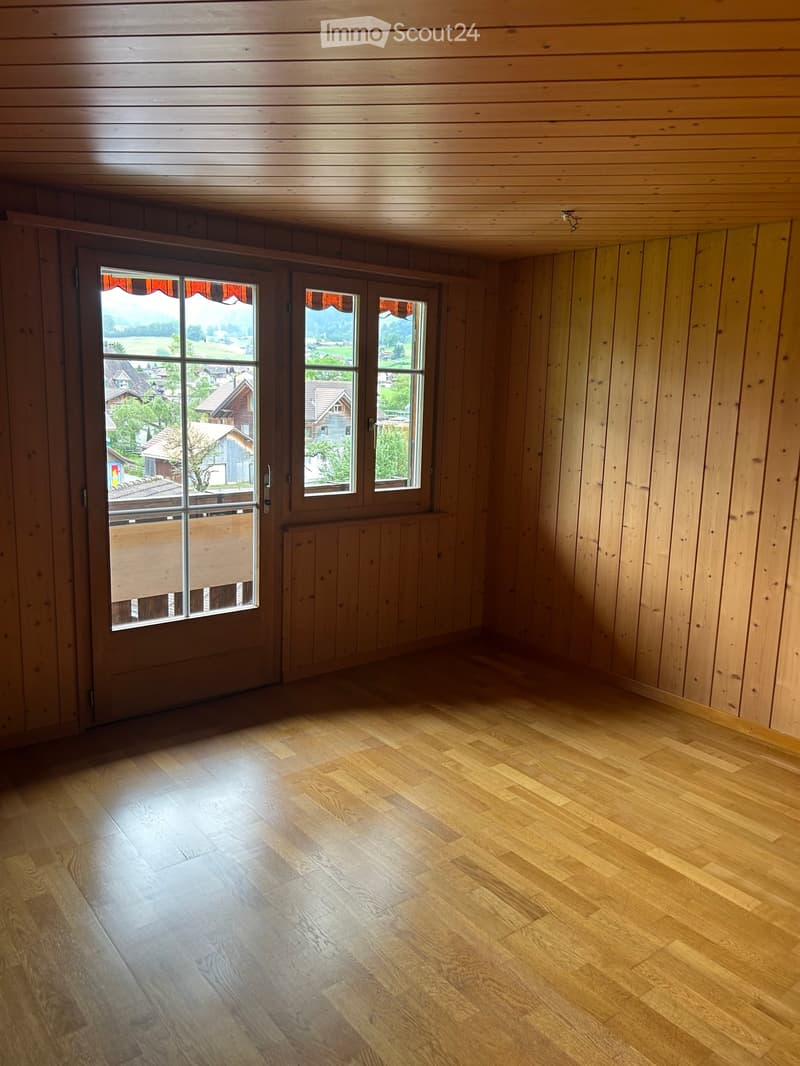 Empty room with wooden walls, wooden floor, and large windows offering a scenic view of the countryside.