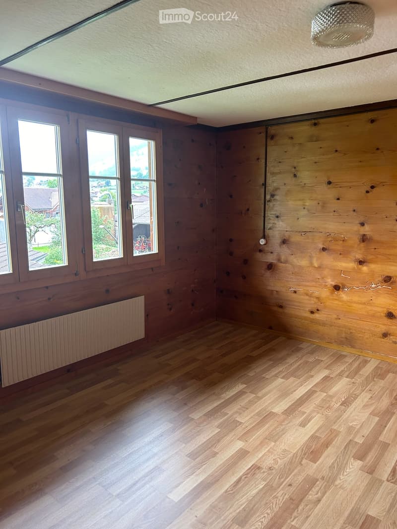 Empty room with wooden flooring, wooden walls, large windows, and a radiator. No furniture or equipment present.