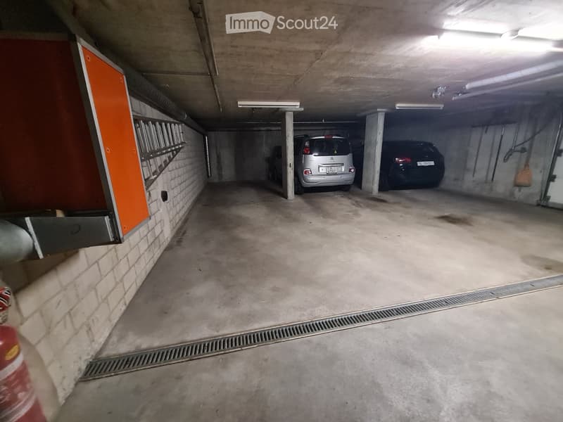 underground parking lot with two cars parked, concrete floor, brick walls, drainage grates, fire extinguisher