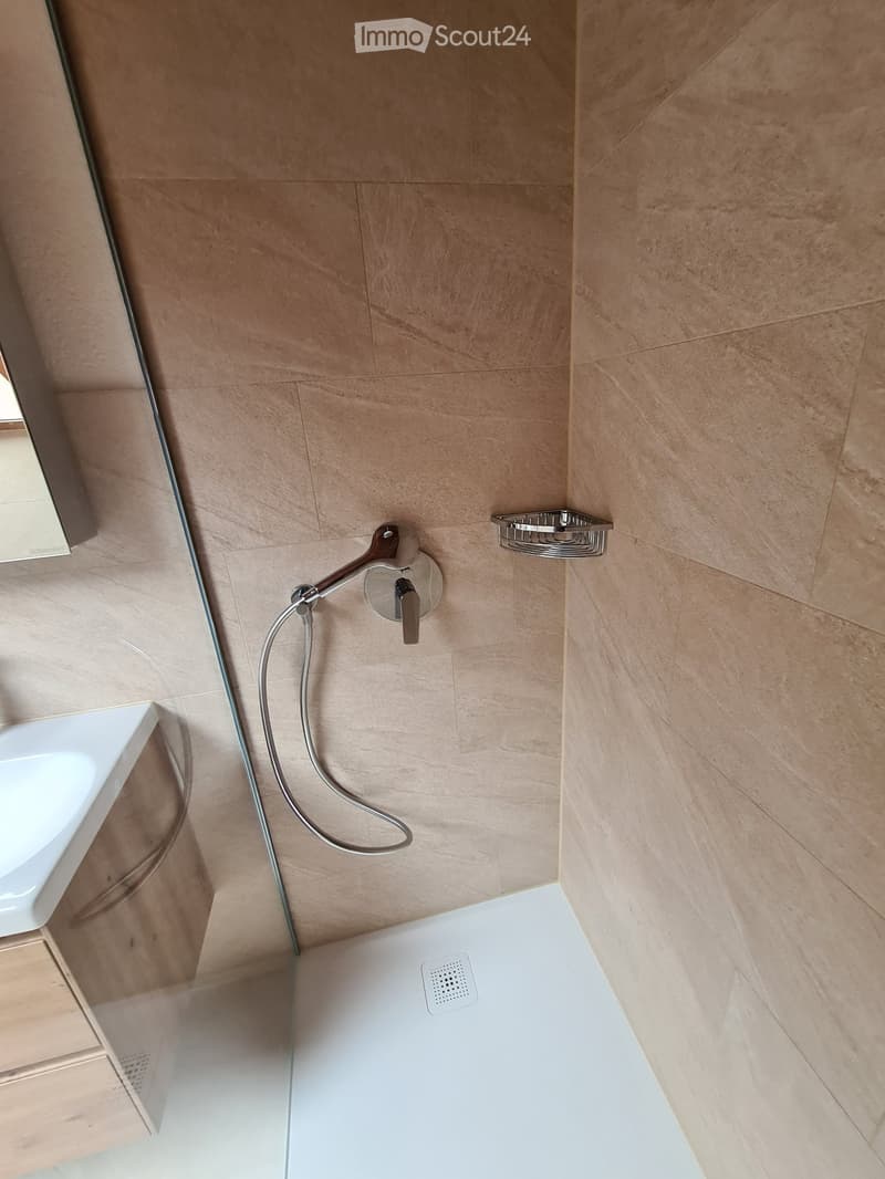 Bathroom with tiled walls, glass shower enclosure, shower head, soap dish, white sink, wooden cabinet