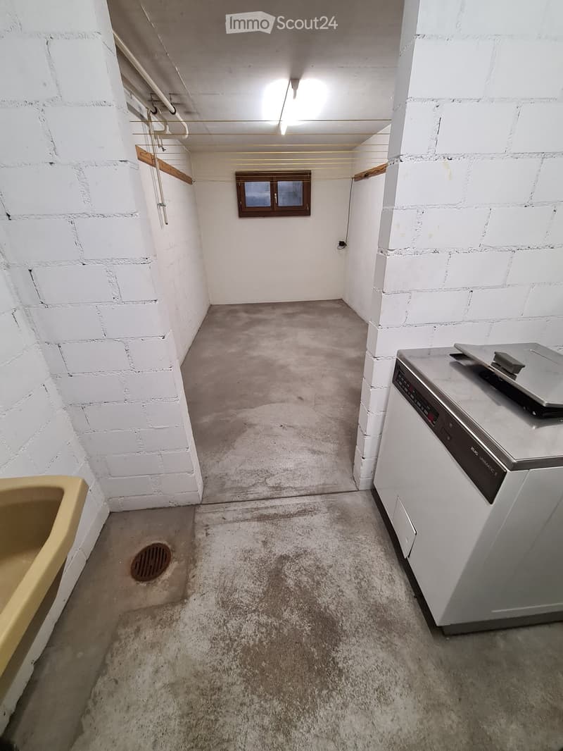 Empty room with white brick walls, concrete floor, small window, and a white washing machine.