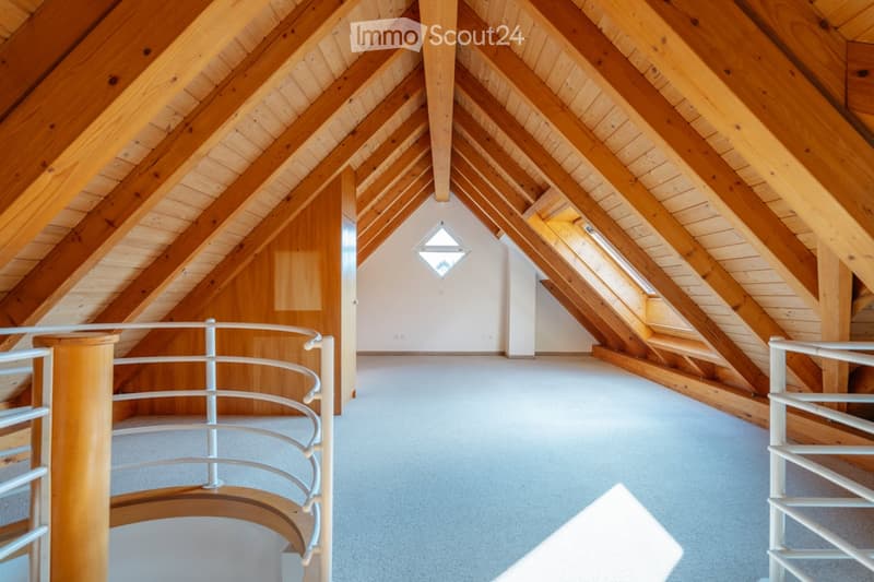 Spacious attic with exposed wooden beams and a curved staircase leading to a small room. The space features a skylight window and a smooth, light-colored floor.