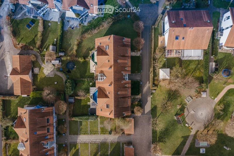 Aerial view of a residential area with multiple houses, red-tiled roofs, gardens, and a swimming pool.