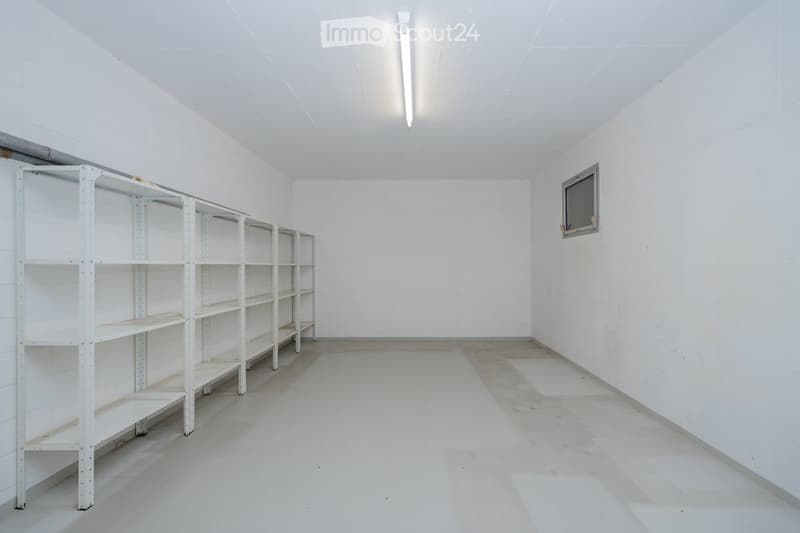 Empty room with white walls, concrete floor, and metal shelving unit on the left side.